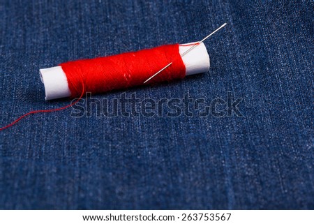 Red thread with needle against a blue jean background.