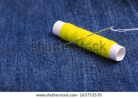 Yellow thread with needle against a blue jean background.