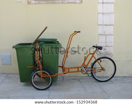 An orange bike with garbage cans parked against a wall