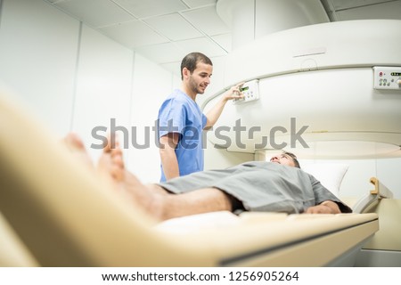 Middle aged patient with cancer and nurse during MRI in hospital lab. Man ins his 40s with doctor in clinic during medical examination. People and disease prevention with magnetic resonance imaging.