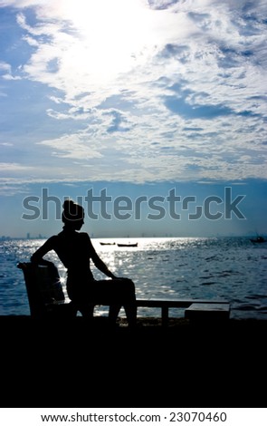 Silhouette of a young woman sitting at the ocean