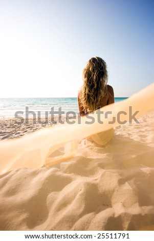 Blonde mermaid sitting on the beach and turned her back