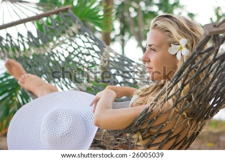 Blonde girl with white flower in hair lying on the hammock