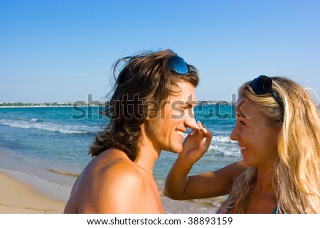 Blonde applying tanning lotion to her boyfriend\'s nose