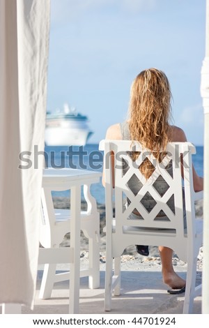Blonde girl with long hair sitting on the white chair in front of the sea with cruise ship on background