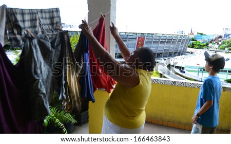 BAHIA, BRAZIL: DECEMBER 8: A resident from the Pepino shanty town hangs up her laundry while a boy looks at the The Itaipava Arena Fonte Nova stadium, on December 08, 2013 in Salvador, Brazil.
