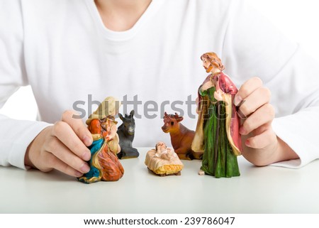 A boy makes a simple Christmas Crib where the little statues represent the Holy Family: the Virgin Mary, Saint Joseph and the infant Jesus, watched by ox and donkey