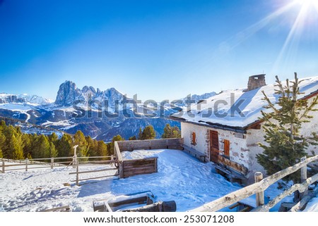 Alpine chalet surrounded by a fence in the snow in front of a panorama of snowy peaks on a bright sunny day in winter on Dolomites Alps