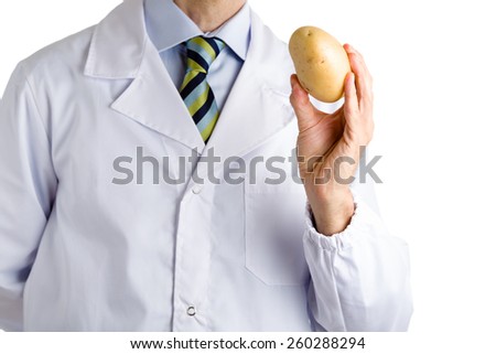 bust of a man wearing medical white coat, light blue shirt and glossy regimental tie white dark blue, light blue and green stripes, and showing a potato  with left hand