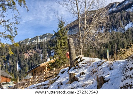 White snowy Dolomites mountains with rocks, snow-capped peaks, wooden cottages and green conifers in winter