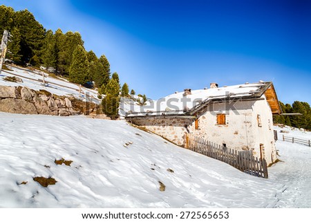 Alpine chalet surrounded by a fence in the snow among snowy peaks and pine forest on a bright sunny day in winter