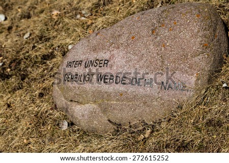 German sentence from The Lord\'s Prayer printed on a rock on winter grass