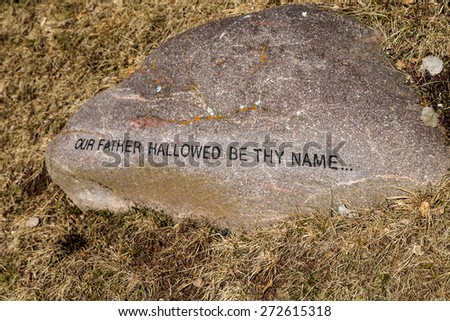 Sentence from The Lord\'s Prayer printed on a rock on winter grass