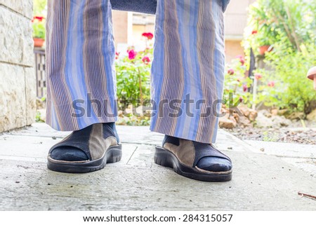 feet of man in brown slippers with blue socks, blue striped pajamas and gray dressing gown in your back yard