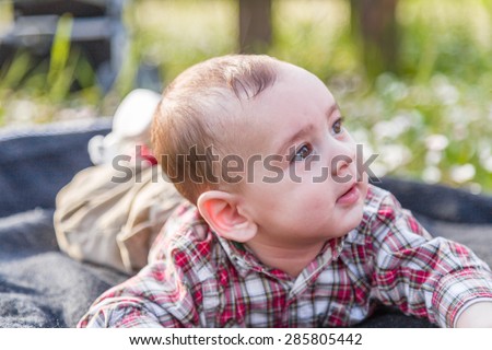The innocent happiness of a cute 6 months old baby with Light brown hair in red checkered shirt and beige pants smiling in a city park