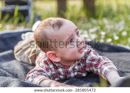 The innocent happiness of a cute 6 months old baby with Light brown hair in red checkered shirt and beige pants smiling in a city park