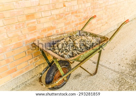 archeology jobs - green wheelbarrow full of grey rocks, stones and rubble