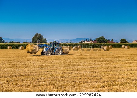 Modern agriculture - after the wheat harvest, the hay round bales are assembled by tractors with forks to be loaded on trucks