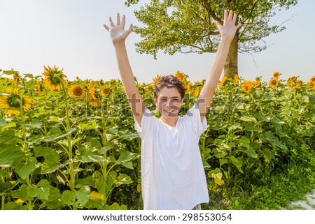 Open air and open arms Ã¢?? Caucasian boy is raising his arms in front of yellow sunflower fields during summer in Italian countryside