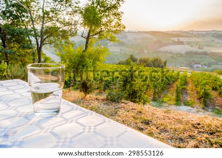 dinner in the country - glass of clear, fresh and sweet water on a table with vineyards, farmlands and green vegetation of the countryside in the background