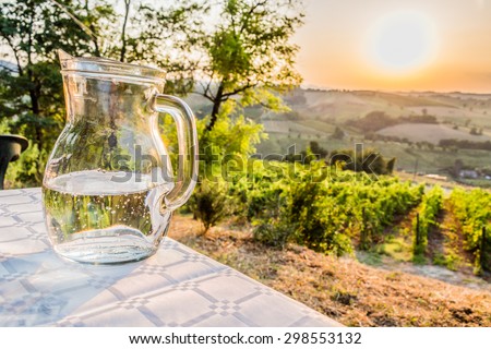dinner in the country - jug of clear, fresh and sweet water on a table with vineyards, farmlands and green vegetation of the countryside in the background