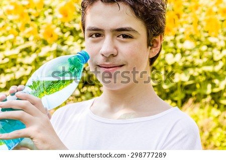 Environmentally-friendly living - Caucasian boy in a field of sunflowers is about to drink clear water from a plastic bottle green bluish to quench thirst on a warm and bright summer day