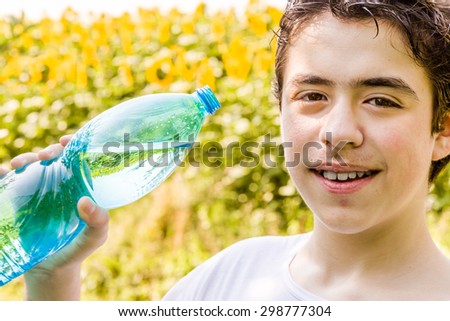 Environmentally-friendly living - Caucasian boy in a field of sunflowers is about to drink clear water from a plastic bottle green bluish to quench thirst on a warm and bright summer day