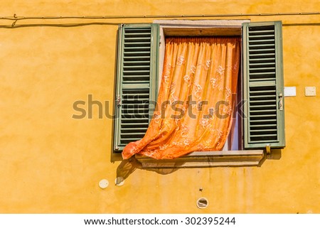 vintage square window with green shutters and orange curtain on deep yellow wall
