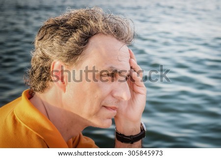 Classy  40 years old sportsman with three-day beard and salt and pepper hair wearing an orange polo shirt while he is thinking in front of the sea