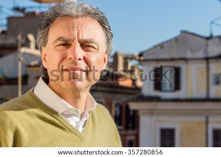 middle-aged man in green polo with the palaces of Rome in the background squints uncomfortable with excessive light of the sun