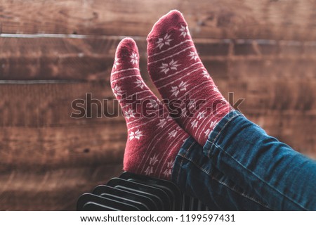 Women's feet in Christmas, warm, winter socks on the heater. Keep warm in the winter, cold evenings. Heating season
