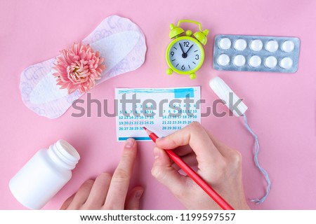 Tampon, feminine, sanitary pads for critical days, feminine calendar, alarm clock, pain pills during menstruation and a pink flower on a pink background. Care of hygiene during menstruation.