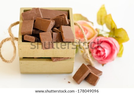 Broken dark chocolate bar in wooden box holder isolated on white background.