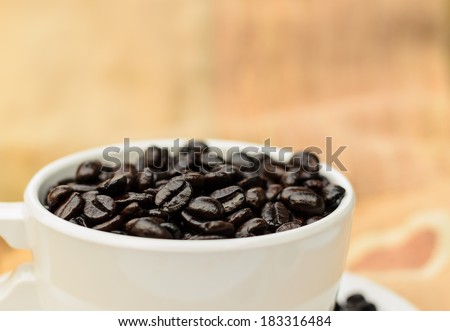 Coffee beans in white coffee cup with beige cloth background.