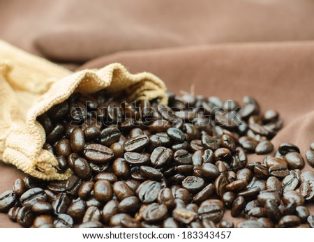 Heap of coffee beans in bag on brown cloth.