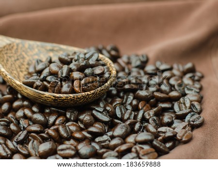 Coffee beans on wooden scoop with brown cloth background.