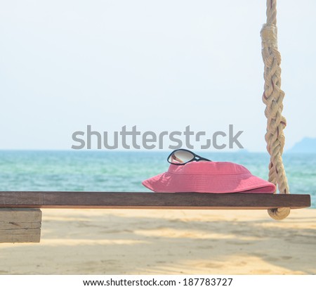 Pink hat and sun glasses on wooden swing at seaside.