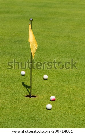 Four golf balls near yellow checkered flag.