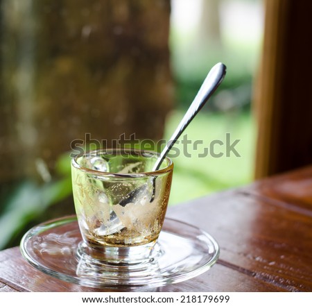 Empty glass coffee cup and metallic spoon on wooden table with green garden background.