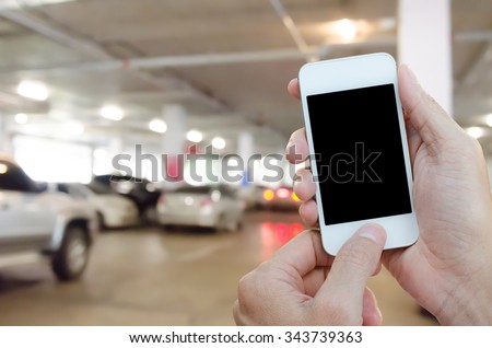 Man hands holding mobile smart phone in indoor car parking.