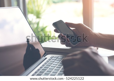 Businessman working on laptop computer and mobile smartphone at home, e commerce or online working, IOT internet of things concept, warm tone.