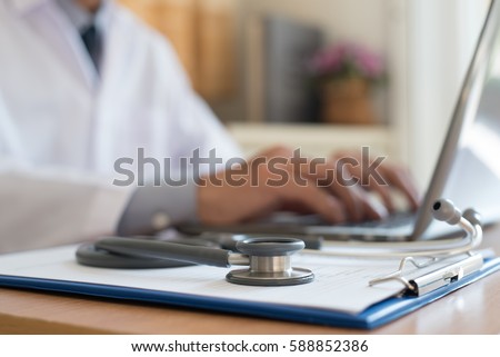 Doctor working on laptop computer and medical stethoscope on clipboard on desk, telemedicine or teleconference, electronics health record system EHRs, electronics medical record system EMRs concept.