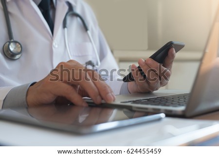 Doctor using mobile smart phone and laptop computer with digital tablet on table on table in hospital room, telemedicine or video conference, Electronic health records system EHRs concept