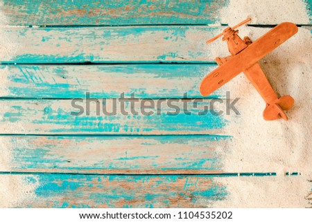 Have a vacation and travel in summer concept - top view of beach sand and toy air plane on wood plank in blue sea paint background.