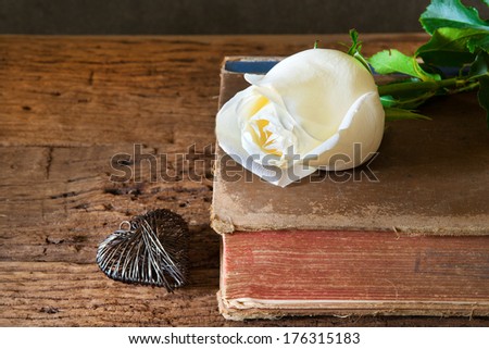 Rose and vintage book, heart on wooden table.