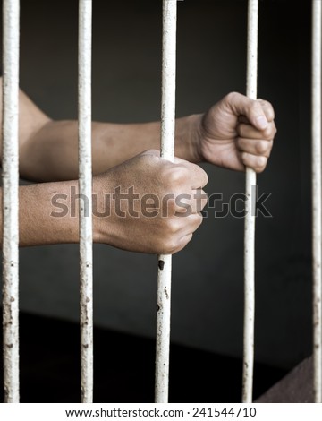 Hands of man prisoner gripping in and out on rusty prison bars