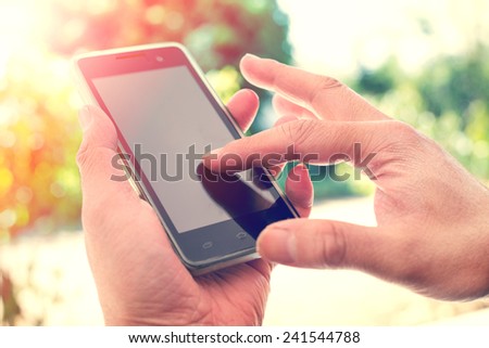 Close up of a man using mobile smart phone outdoor,  nature background. (vintage color tone)