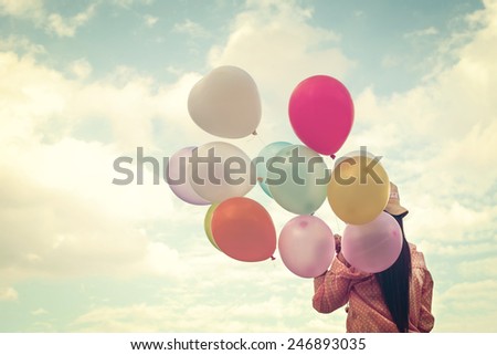 Vintage photo of  Happy young girl  holding colorful balloons and flying on clouds sky background.