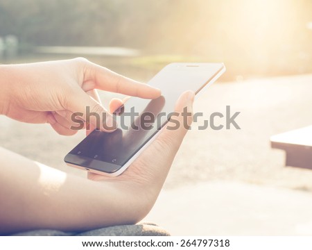 Close up of a woman using mobile smart phone outdoor, nature background. (vintage color tone)