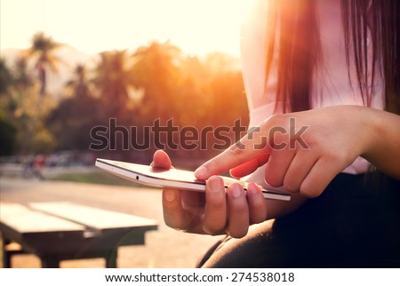 Close up of a woman using mobile smart phone in sunset with outdoor, nature background. (vintage color tone)
